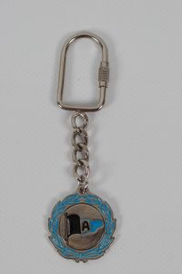 Metallischer Schlüsselanhänger mit einer Flagge und einem blauen Kranz um das Emblem.