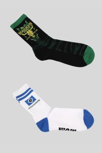 Zwei Paar Socken, eines mit Wacken-Logo in Schwarz und Grün, das andere mit HSV-Logo in Weiß und Blau.